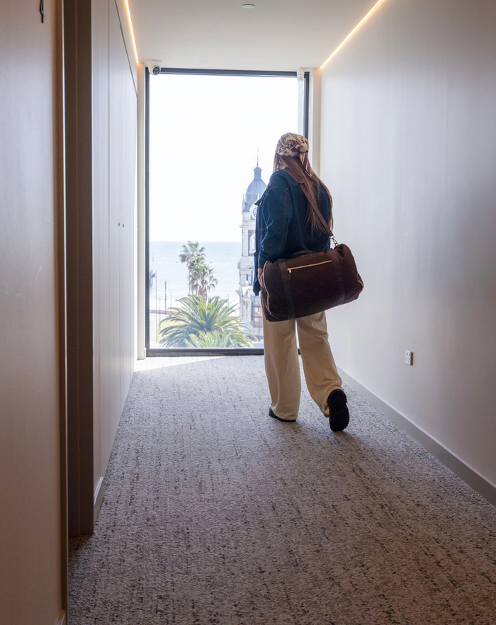 A traveller walking down a hotel corridor with her GLASARI duffle