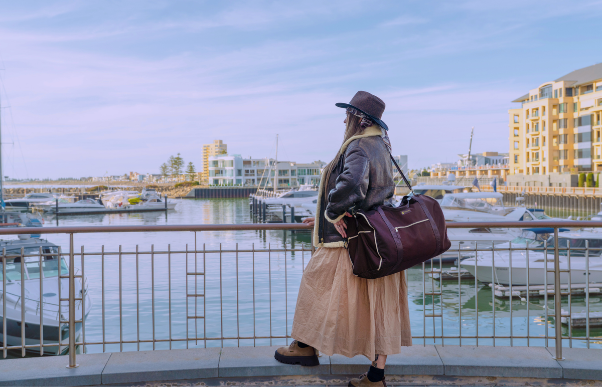 A traveller walking along the marina with a GLASARI Retreat Duffle over her shoulder