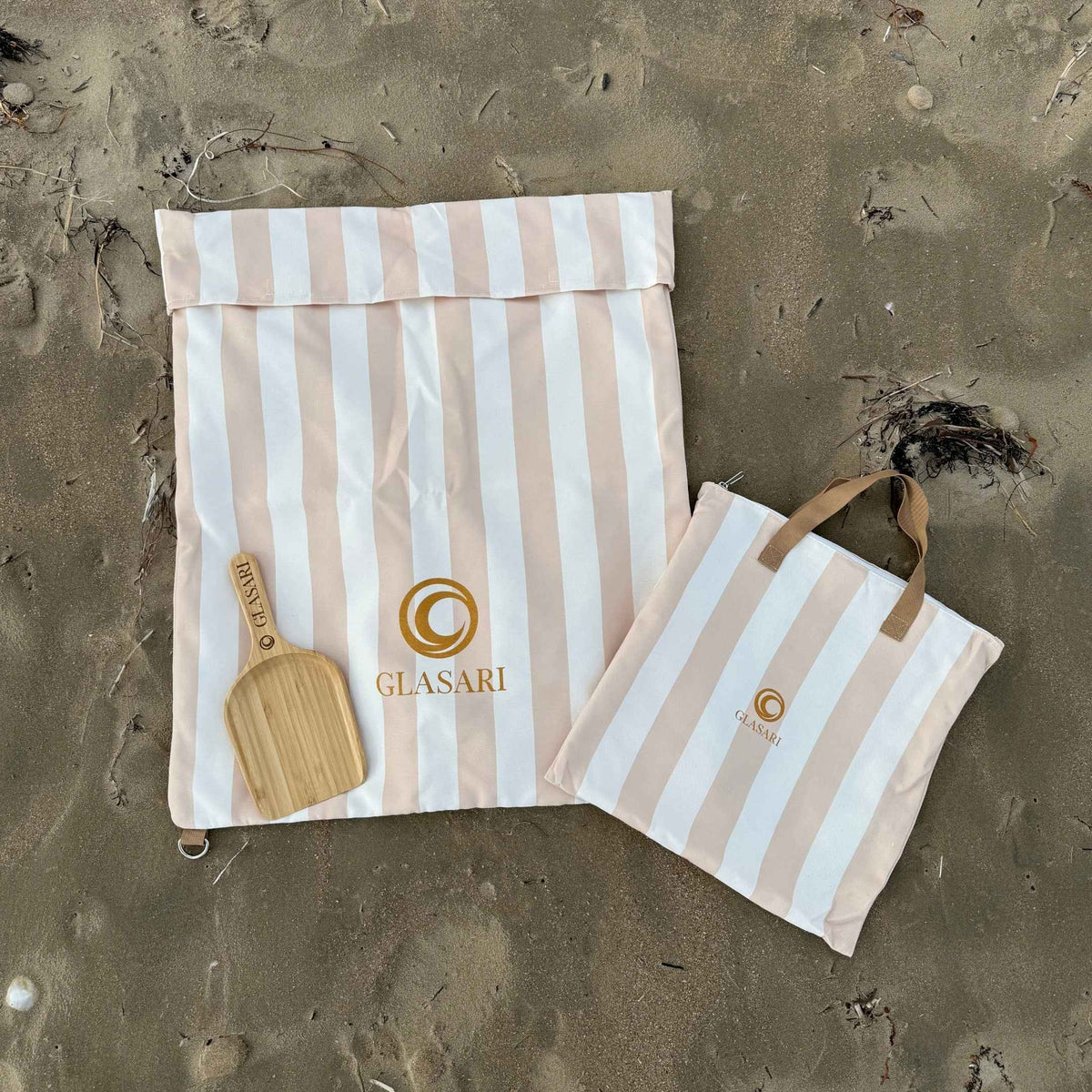 GLASARI Beach Buddy Vault in Coastal Sand stripe laid flat and empty, with its matching zip carry bag and the free bamboo scoop on the sand