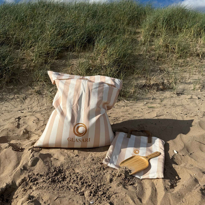 The cream and sand striped Beach Buddy Vault on the sand with its wooden sand brush