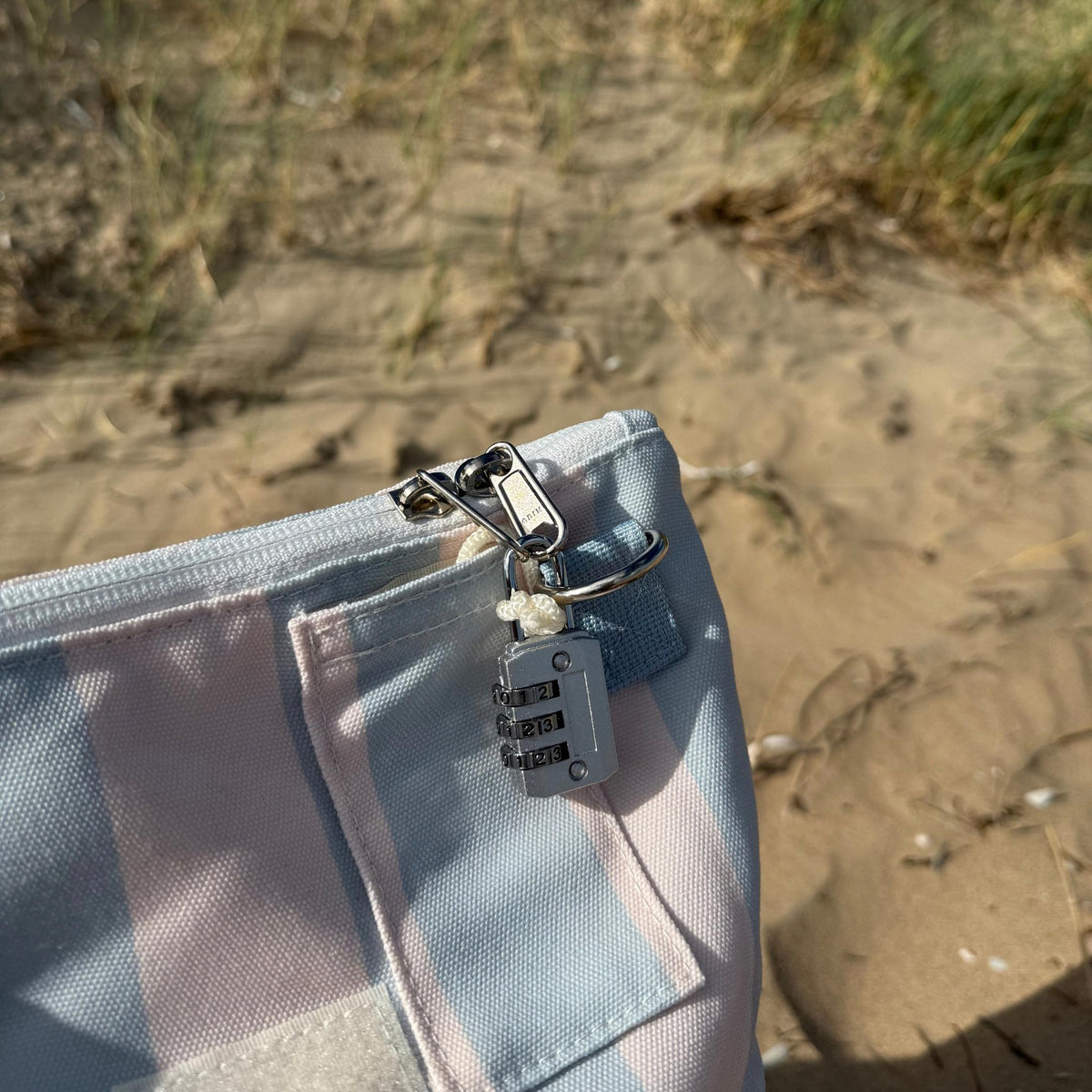GLASARI Beach Buddy Vault in Blue Horizon stripe on the sand, with its combination lock clipped to the zip