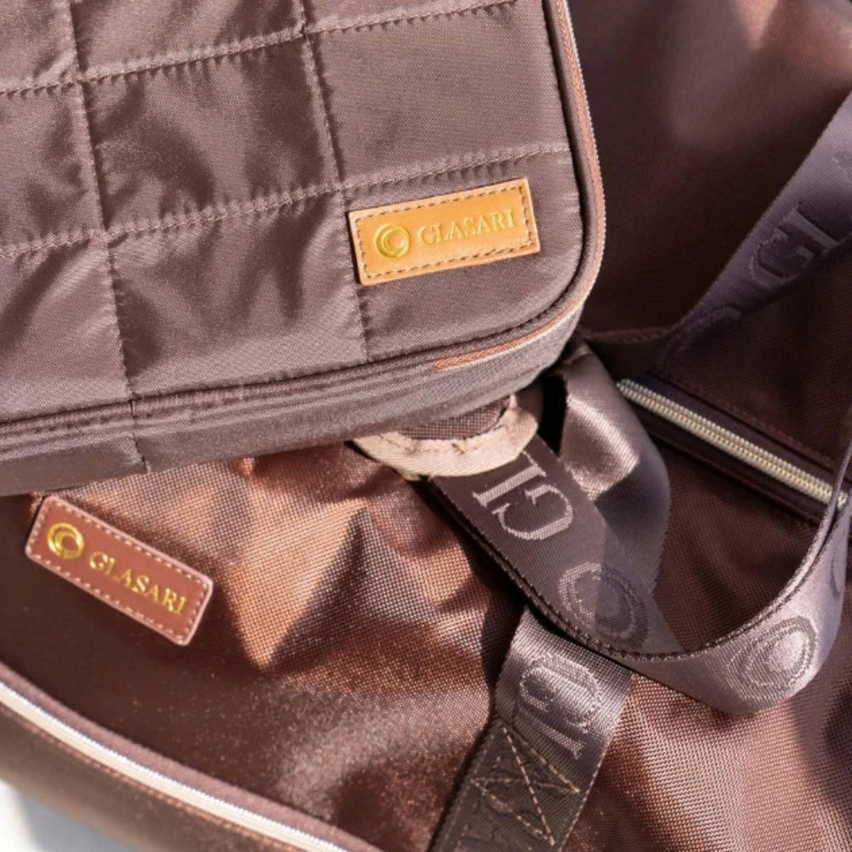 GLASARI On-The-Glow Cosmetic Case in Cocoa Drift resting on the Retreat Duffle in Cocoa Drift, close-up of the quilted finish and leather GLASARI labels